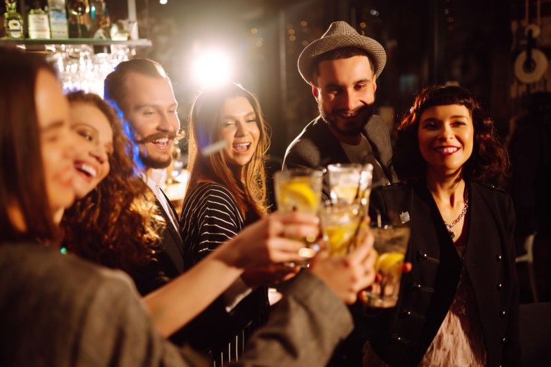Group of smiling people raising glasses in a bar.