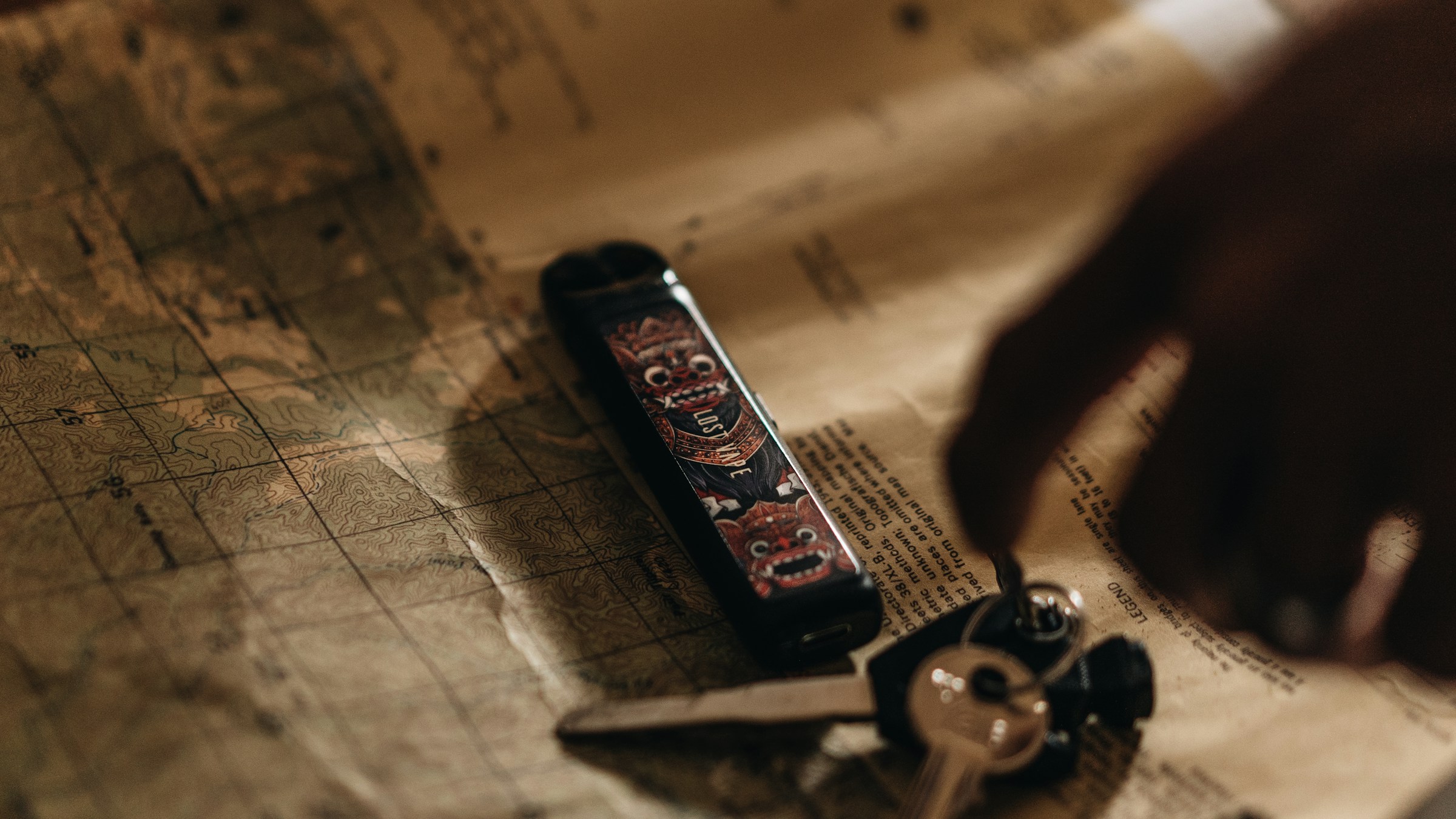 eka-rizal-fikri-CZpBcFNyXv4-unsplash (2) Keys and a vape device on a map, with a hand reaching in.