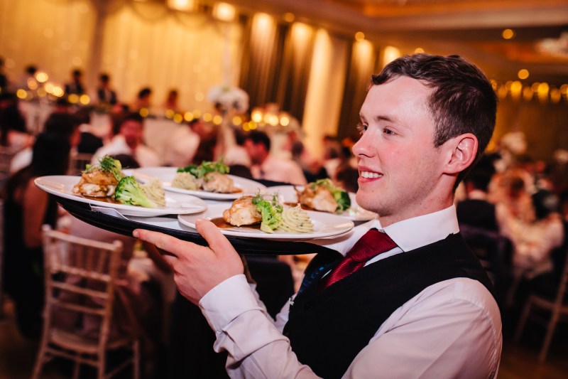 Waiter carrying multiple plates of food at a busy banquet event.