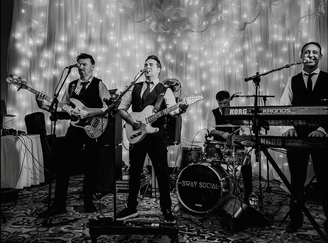 Four musicians perform on stage with instruments in front of a lit backdrop.