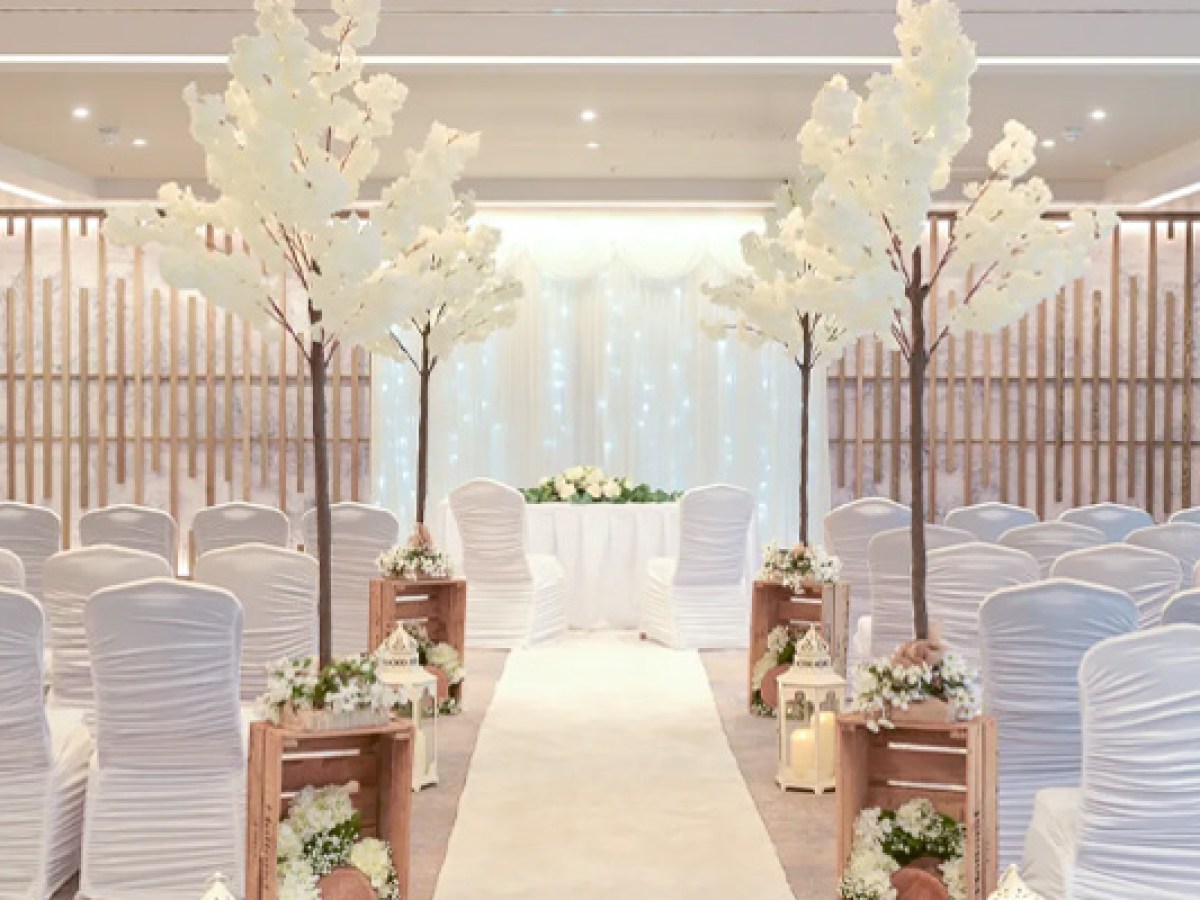 Indoor wedding aisle with white chairs, floral decorations, and wooden accents.