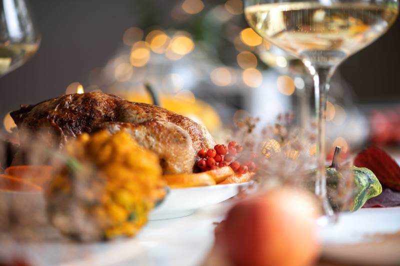 Festive table with roasted meat, squash, berries, and wine glasses.
