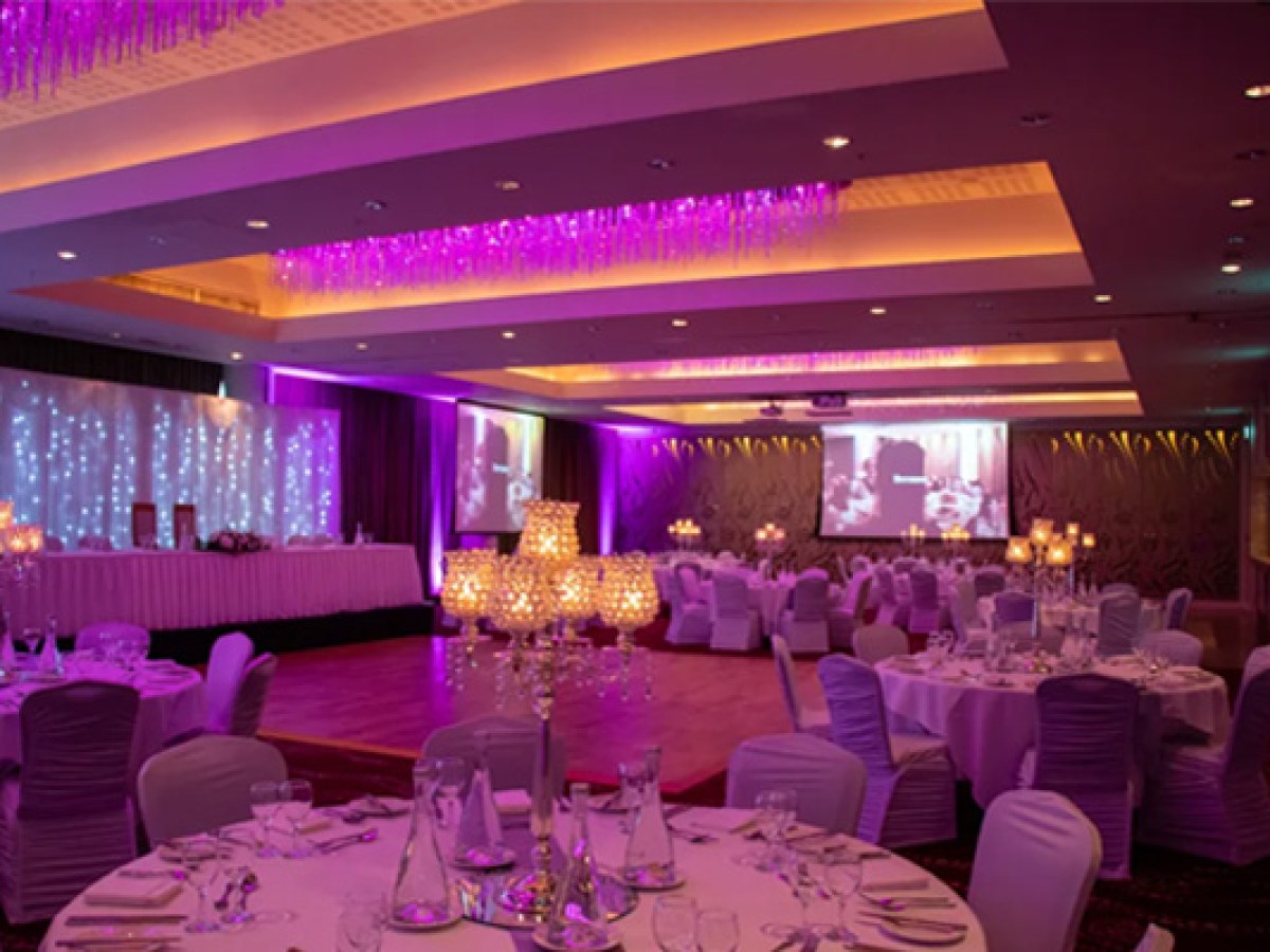 Elegant banquet hall with purple lighting, round tables, and chandeliers.